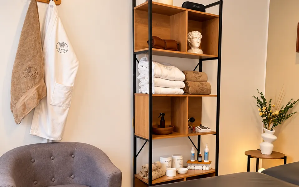 Estantería de madera con toallas, productos y la bata de Eunoia en una cabina.